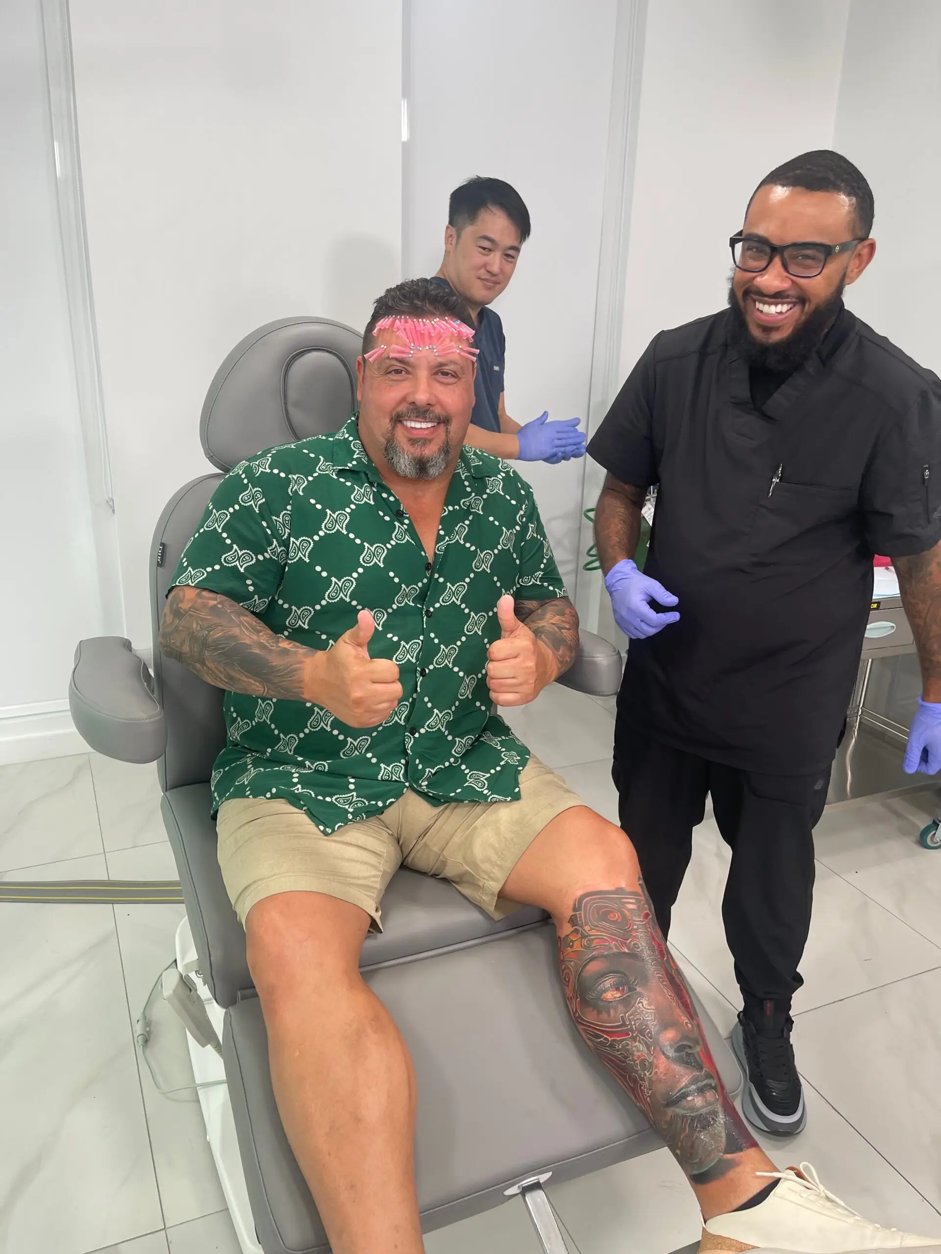 a man sitting in a chair with a man with tattoos on his head